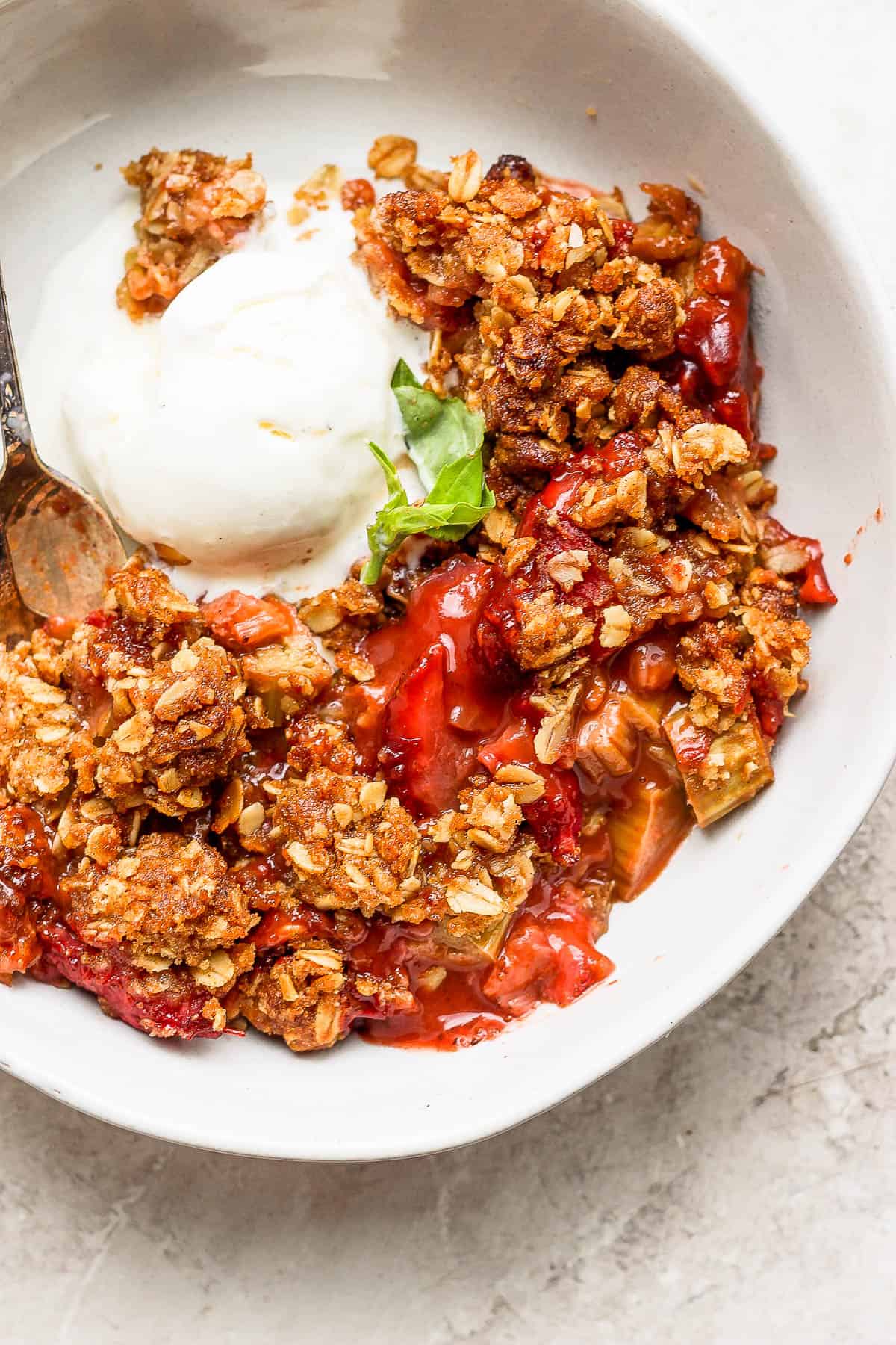 Strawberry rhubarb crisp topped with a scoop of vanilla ice cream in a bowl.