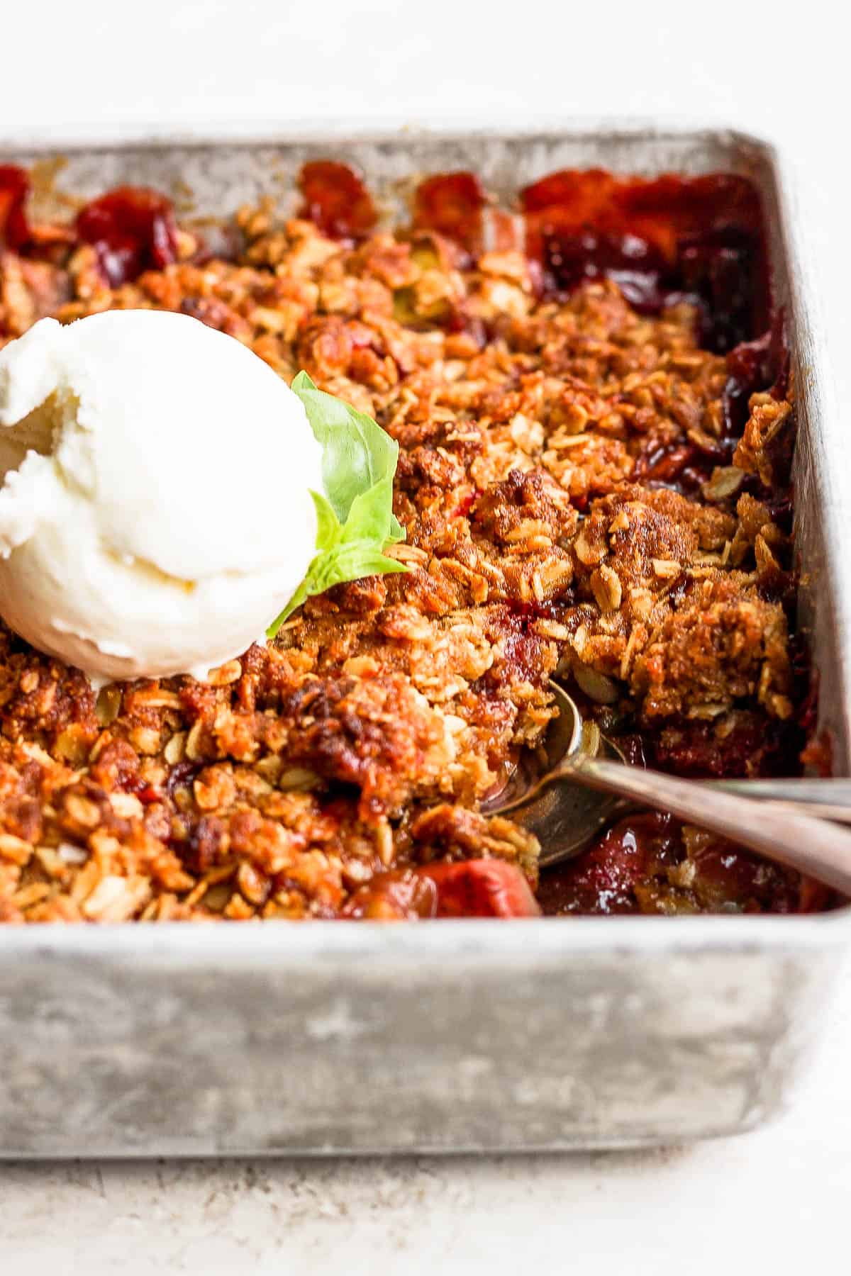 Strawberry rhubarb crisp in a baking pan topped with vanilla ice cream.
