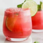 A glass of a watermelon cocktail with lime garnish.