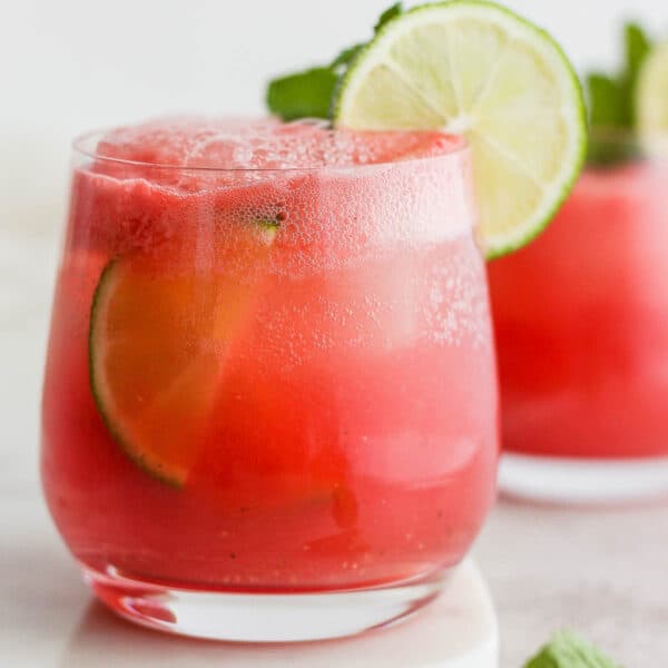 A glass of a watermelon cocktail with lime garnish.