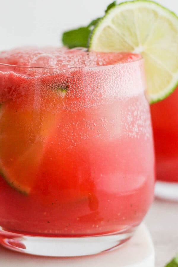 A glass of a watermelon cocktail with lime garnish.