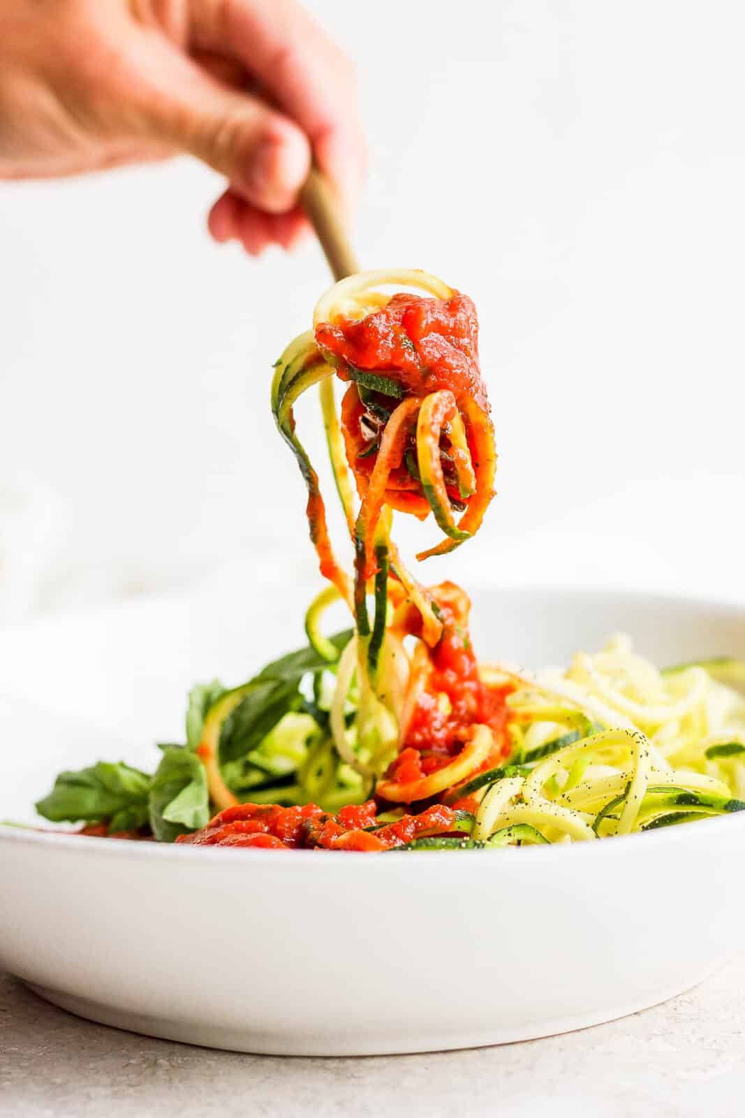 A fork pulling some of the zucchini spaghetti up and out of the bowl.