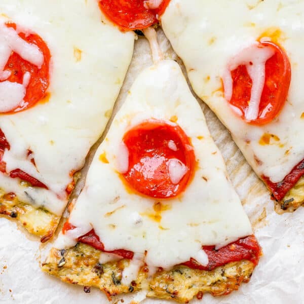 A cauliflower pizza crust topped with cheese and pepperoni with one slice being pulled out.