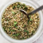 Top shot of a small jar of homemade italian seasoning with a spoon sticking out.