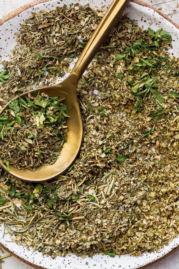 Plate filled with homemade italian seasoning with gold spoon.