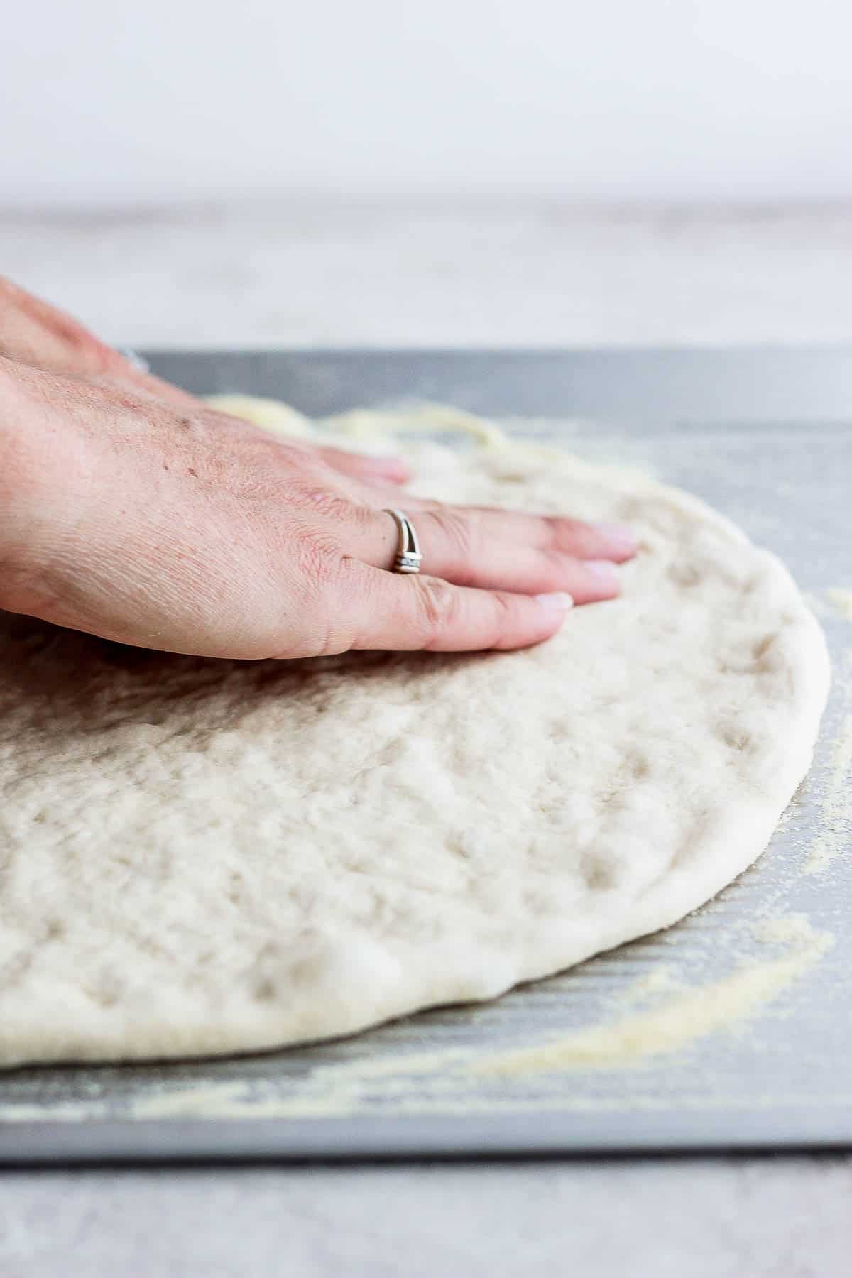 Side angle of someone pressing out pizza dough on a flat cookie sheet. 