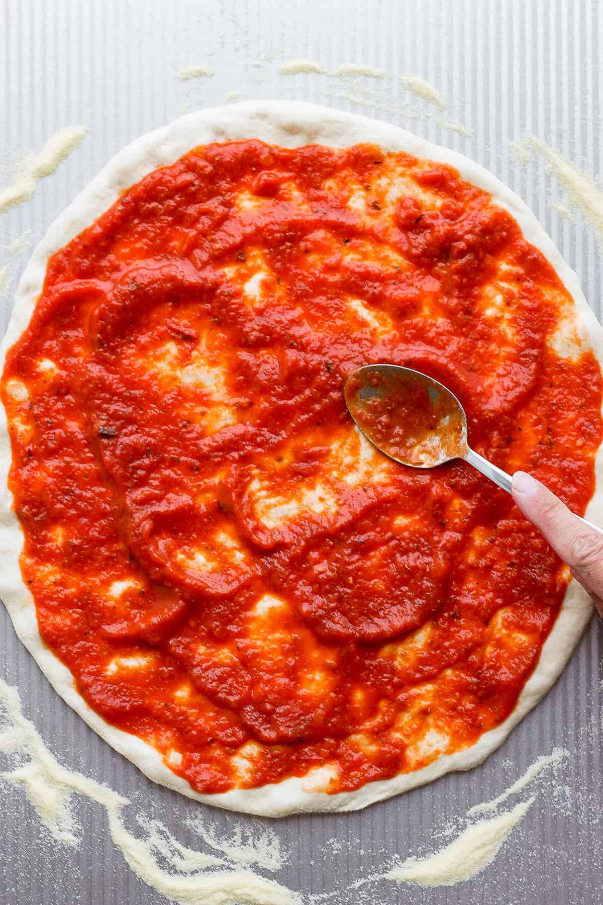 Someone spreading out pizza sauce on pizza dough. 