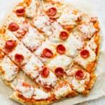 A pepperoni pizza, made on homemade pizza dough, cut into squares on a piece of parchment paper.