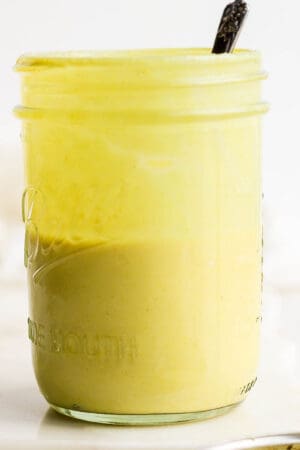 Mason jar of honey mustard dressing with spoon sticking out.