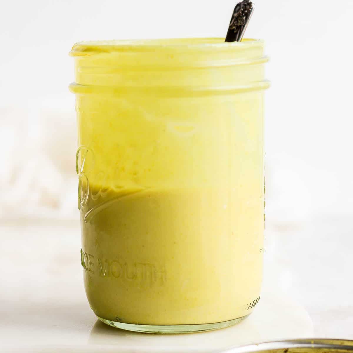 Mason jar of honey mustard dressing with spoon sticking out.