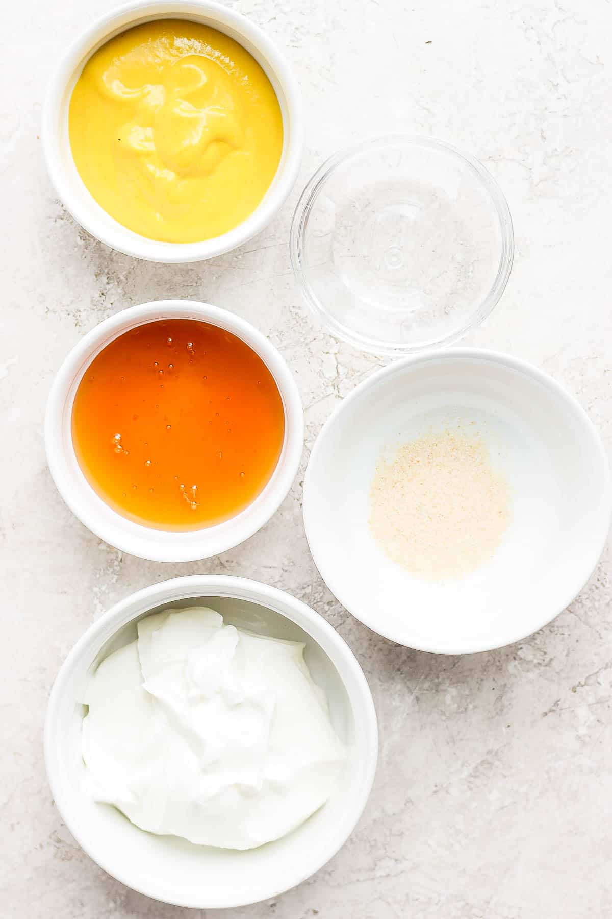 Ingredients for honey mustard dressing in separate bowls.