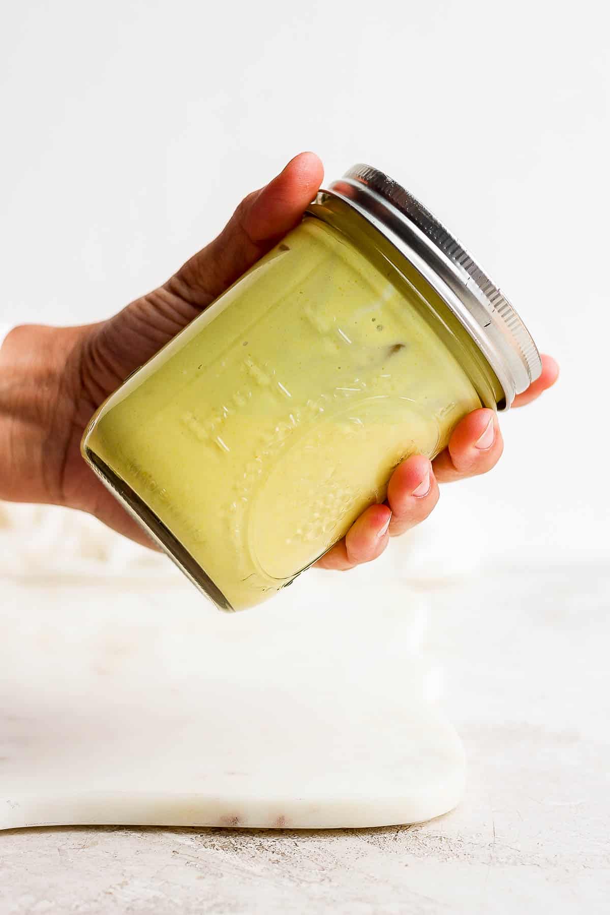 A hand shaking honey mustard dressing in a mason jar.