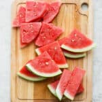 Wooden cutting board with various examples of how to cut watermelon (wedges and sticks).