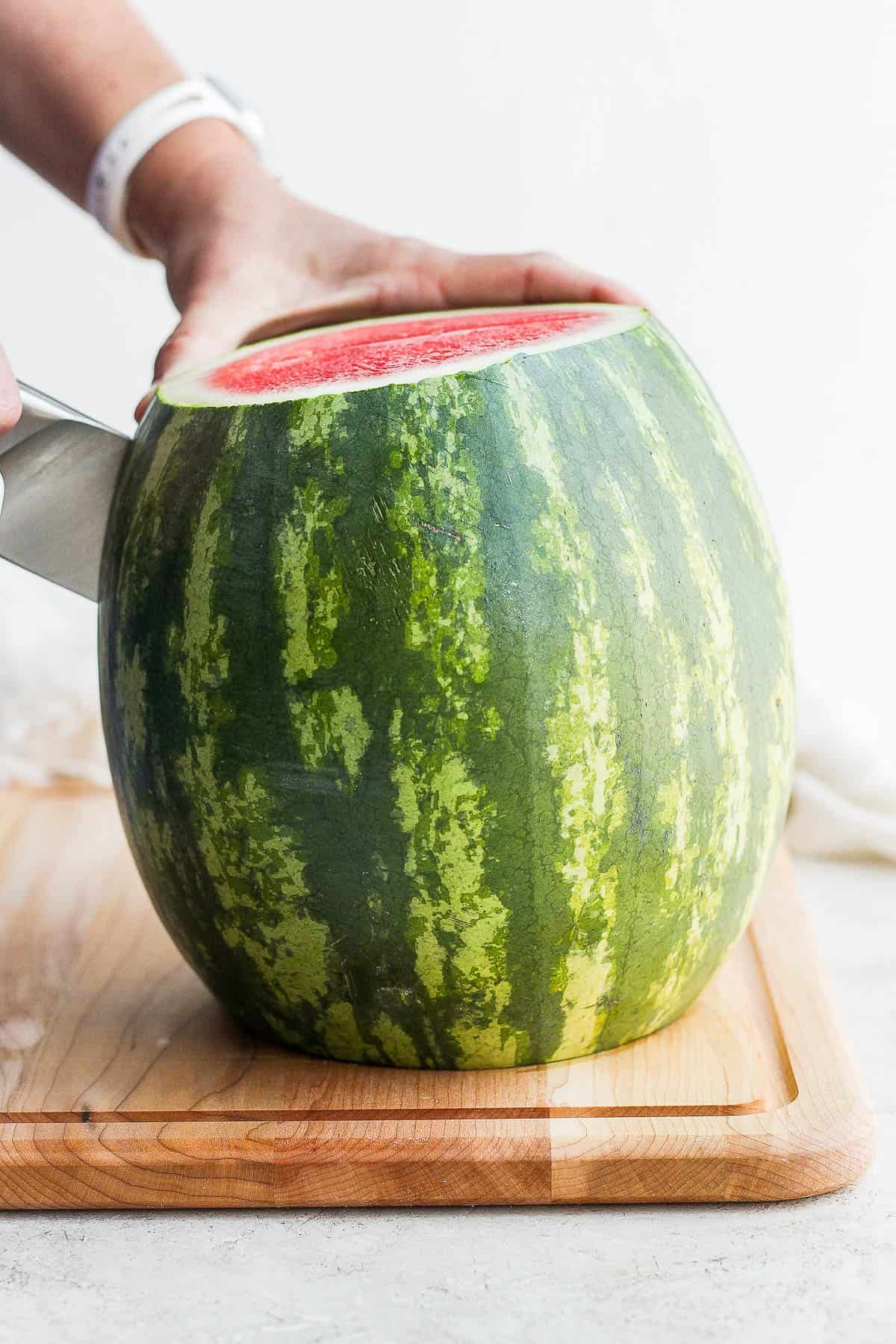 A whole watermelon being cut in half, lengthwise.