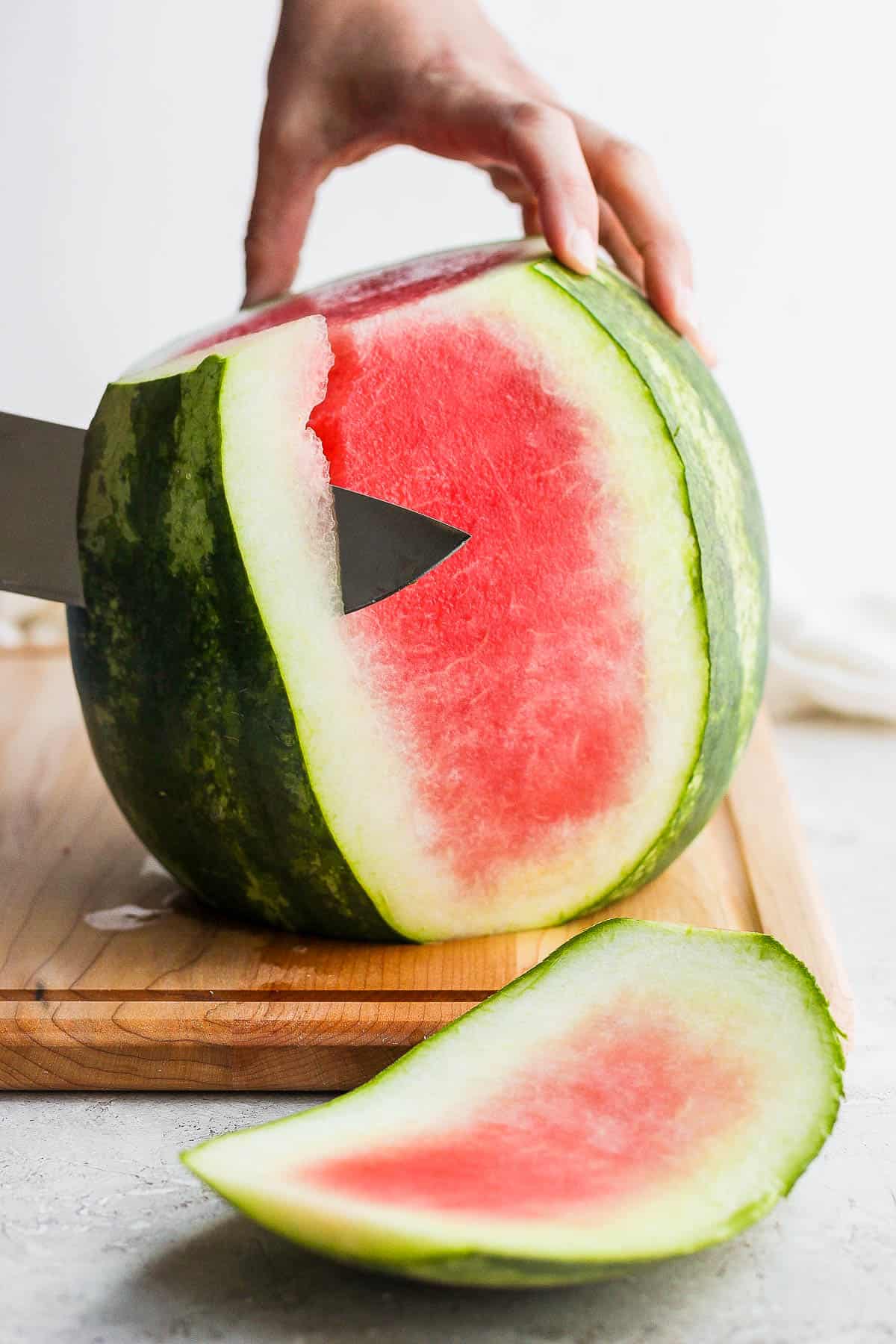 A large knife slicing the rind off a watermelon.