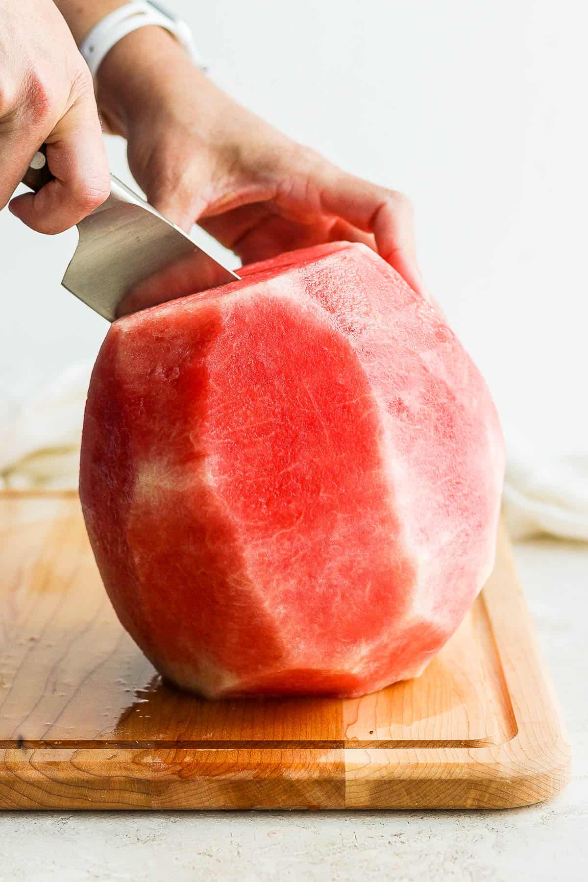 Watermelon, with the rind cut off, being cut in half.