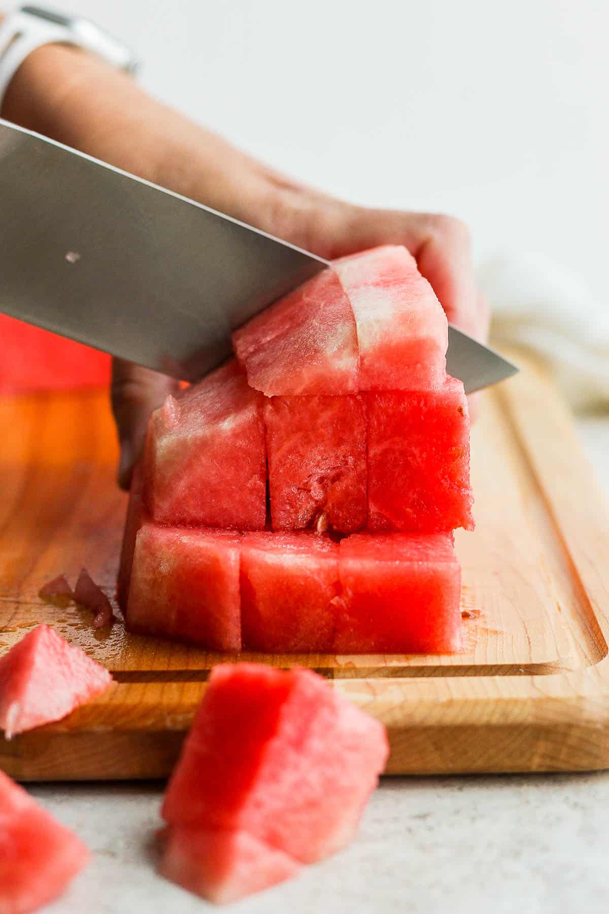 A large piece of watermelon being cut into cubes on a cutting board.