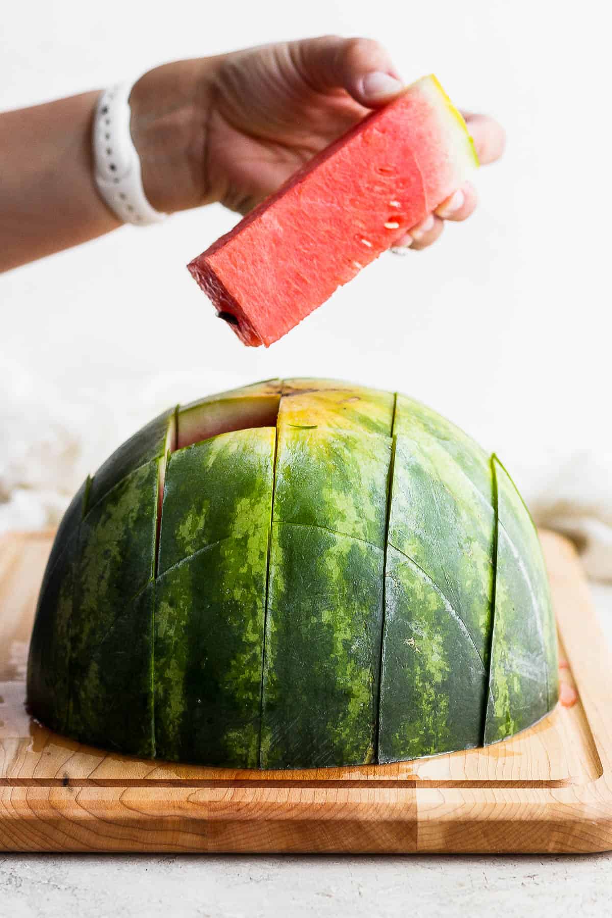 A hand pulling a stick out of a watermelon half.