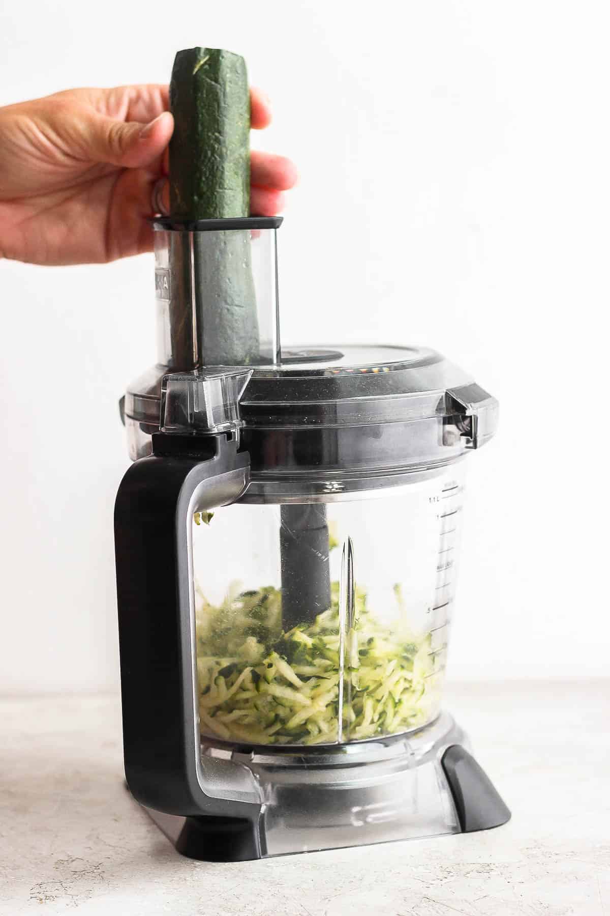 Zucchini being grated with a food processor. 