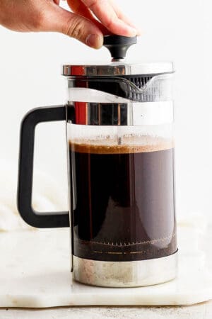 Someone pressing down on a french press coffee maker plunger as they make coffee in a french press.