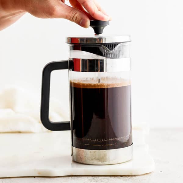 Someone pressing down on a french press coffee maker plunger as they make coffee in a french press.
