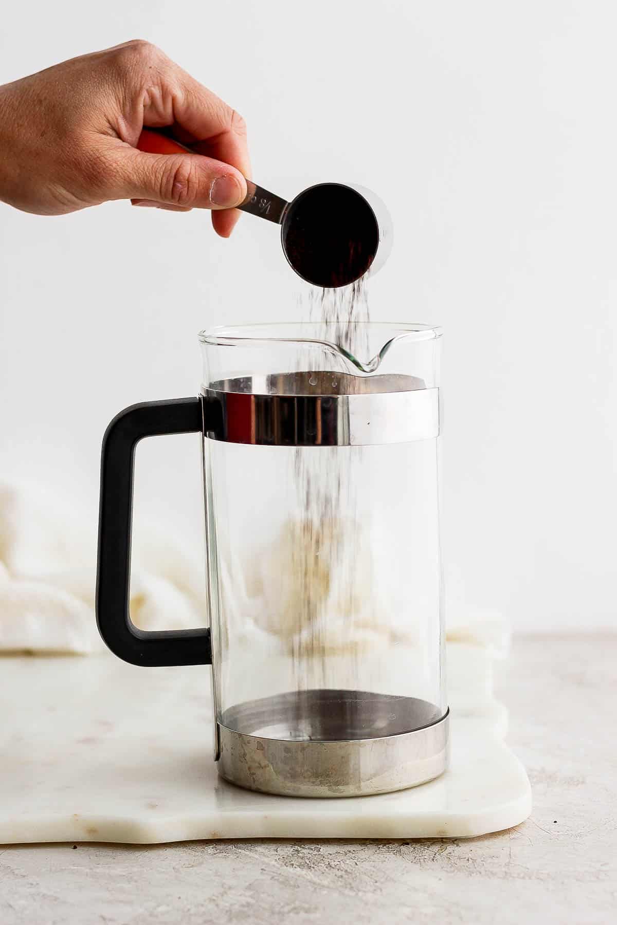 Someone pouring a scoop of coarse coffee grounds into a french press.