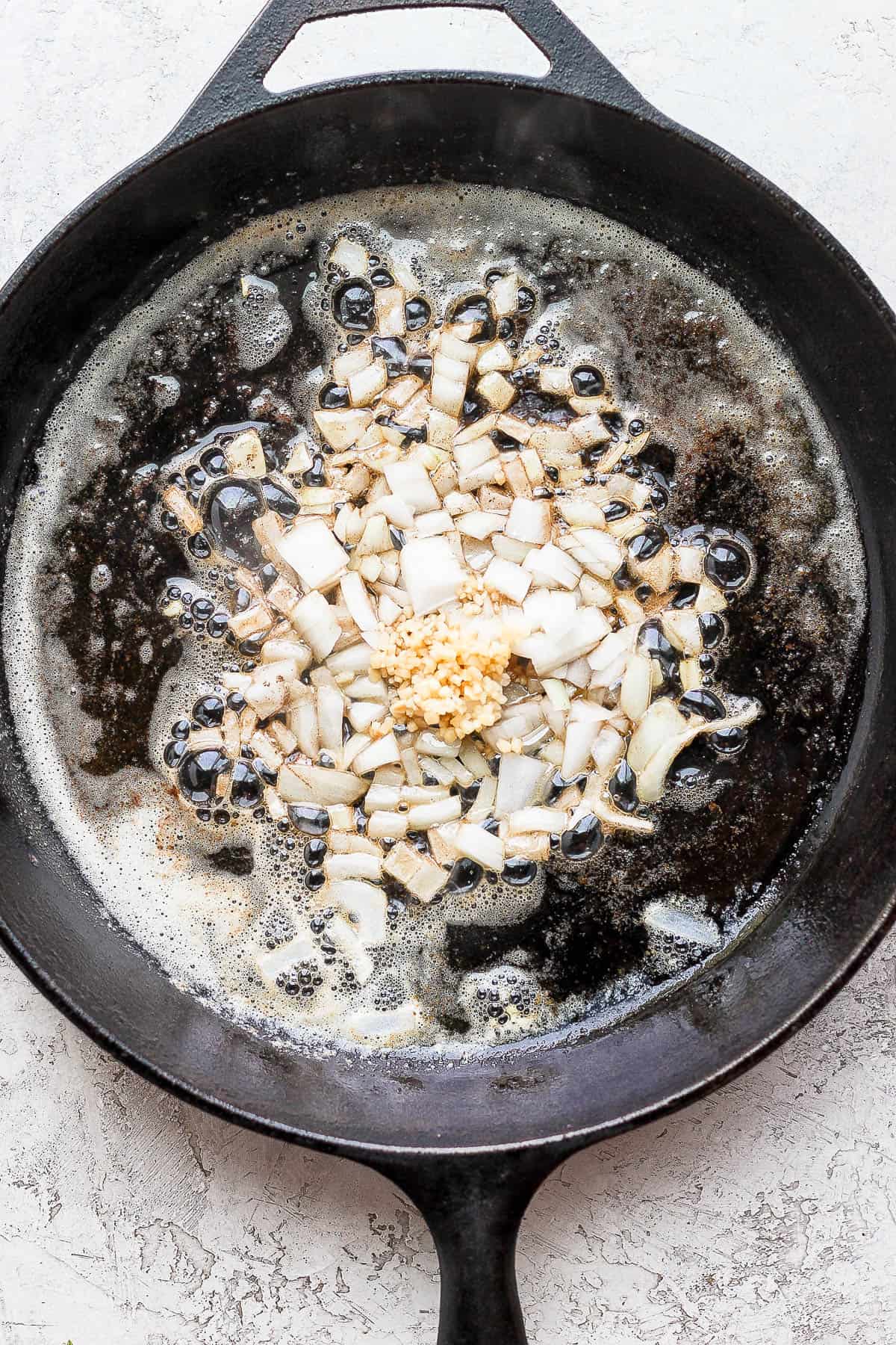 A cast iron pan with onions and garlic cooking in butter.