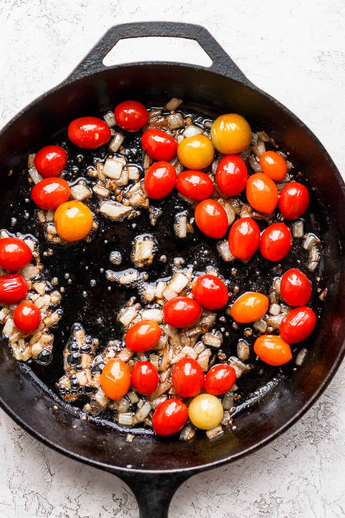 Cherry tomatoes beginning to burst in the skillet.