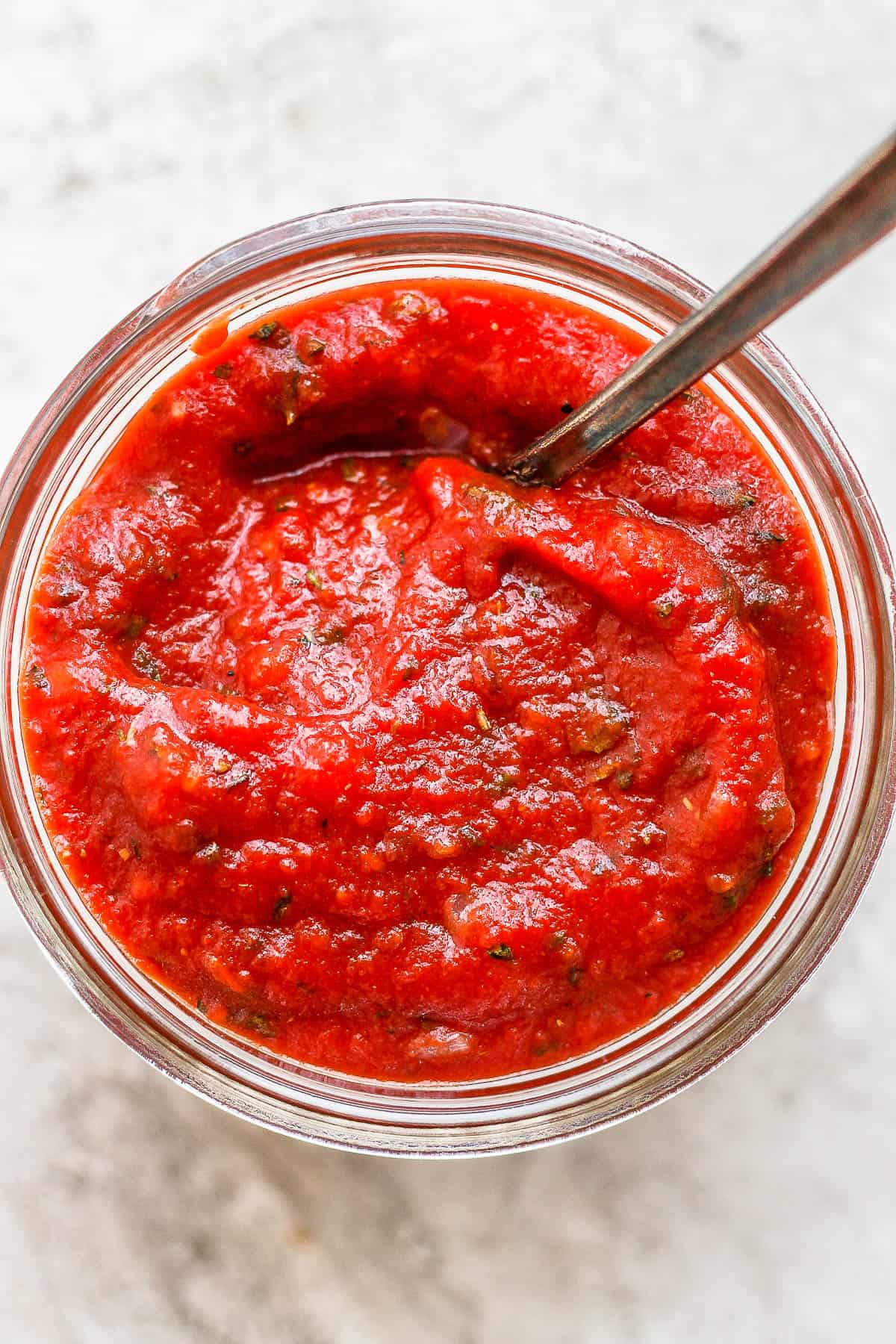 Homemade pizza sauce in a mason jar with a spoon.