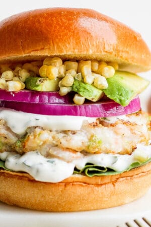 A shrimp burger on a bun with onion, corn, avocado and cilantro lime crema.