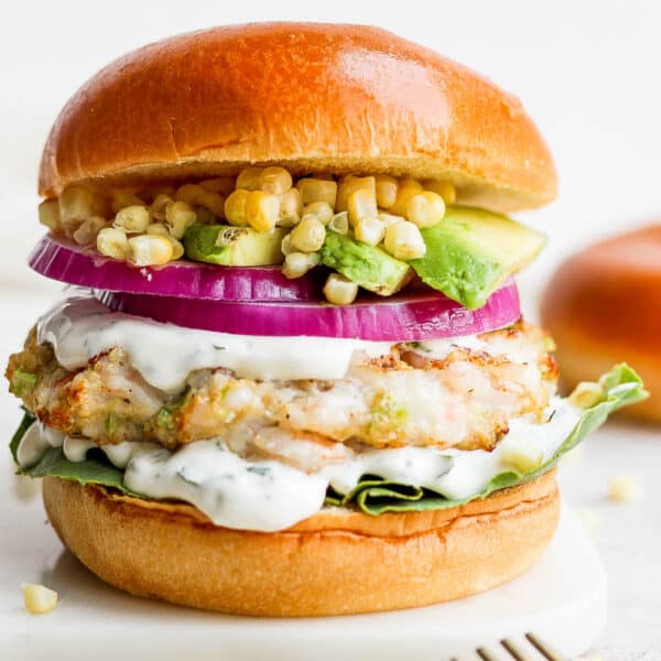 A shrimp burger on a bun with onion, corn, avocado and cilantro lime crema.