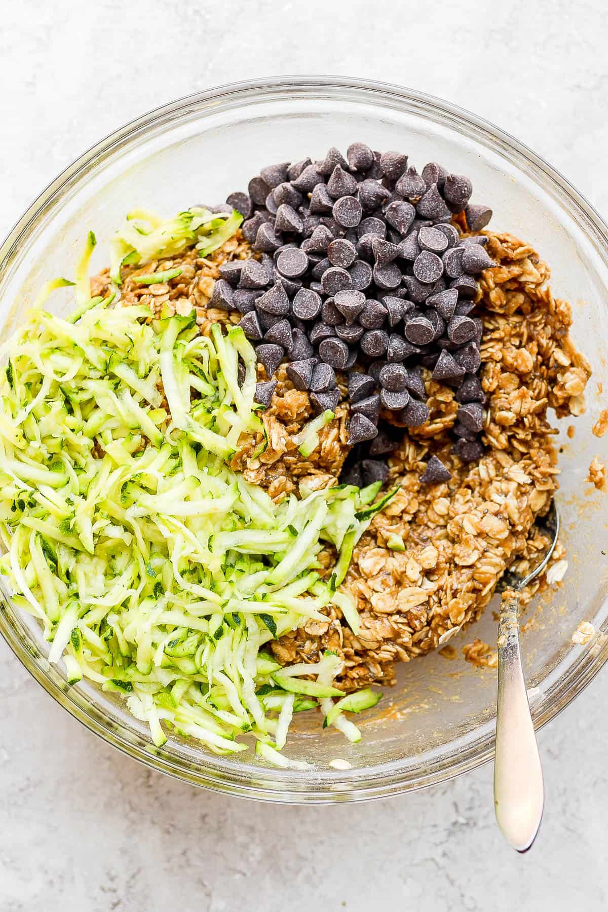 Shredded zucchini and chocolate chips being added to the dough.