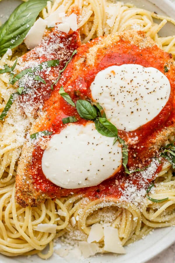 A plate of spaghetti noodles and a piece of baked chicken parmesan.