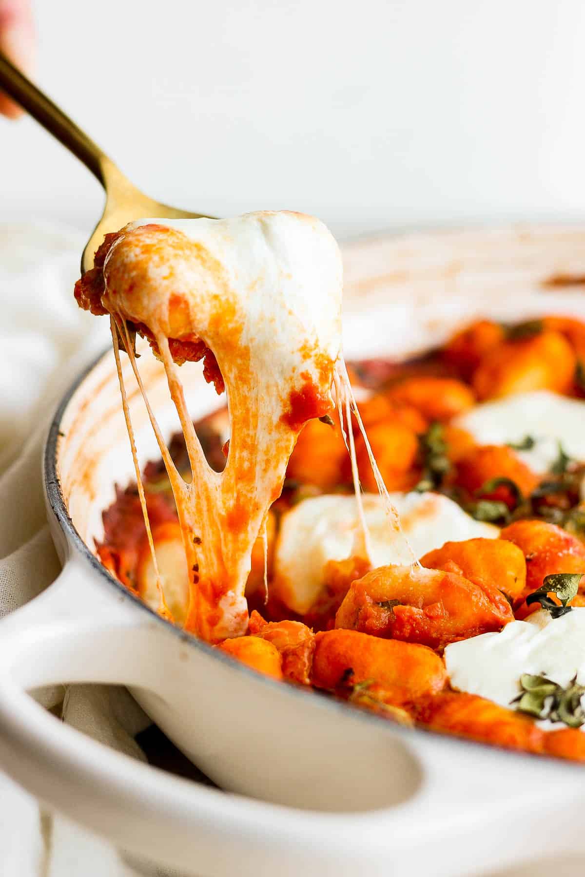 A spoon pulling some of the baked gnocchi out of the pan.