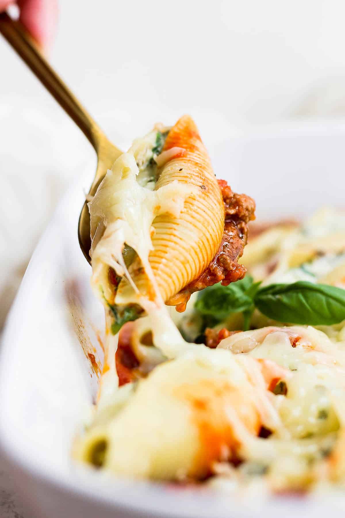 A stuffed shell on a fork being pulled away from the main dish. 