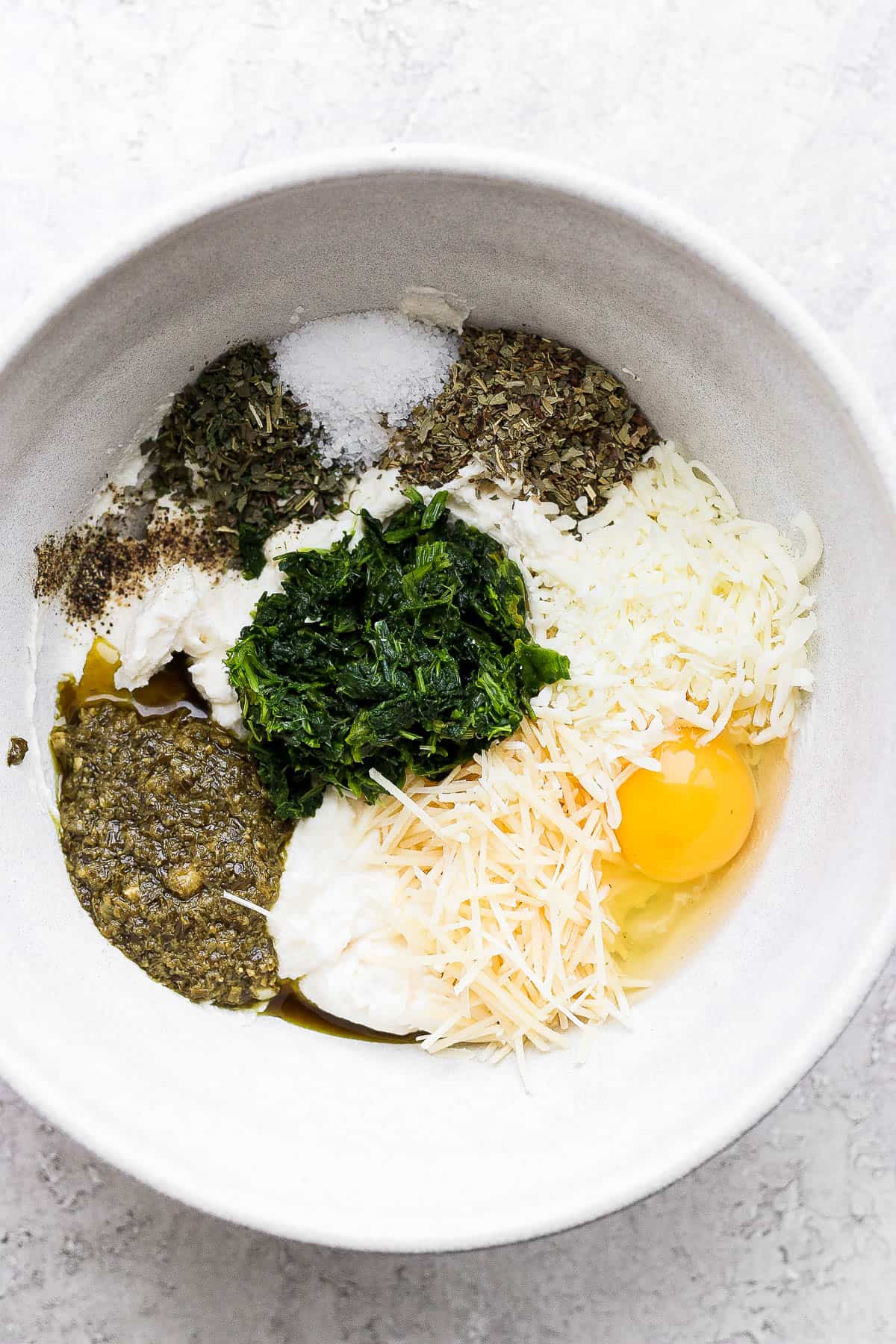 Ingredients for the ricotta cheese placed in a medium sized bowl: ricotta cheese, chopped spinach leaves, pesto, parmesan cheese, mozzarella cheese, lemon juice, Italian seasoning, fresh basil, egg, salt and pepper.