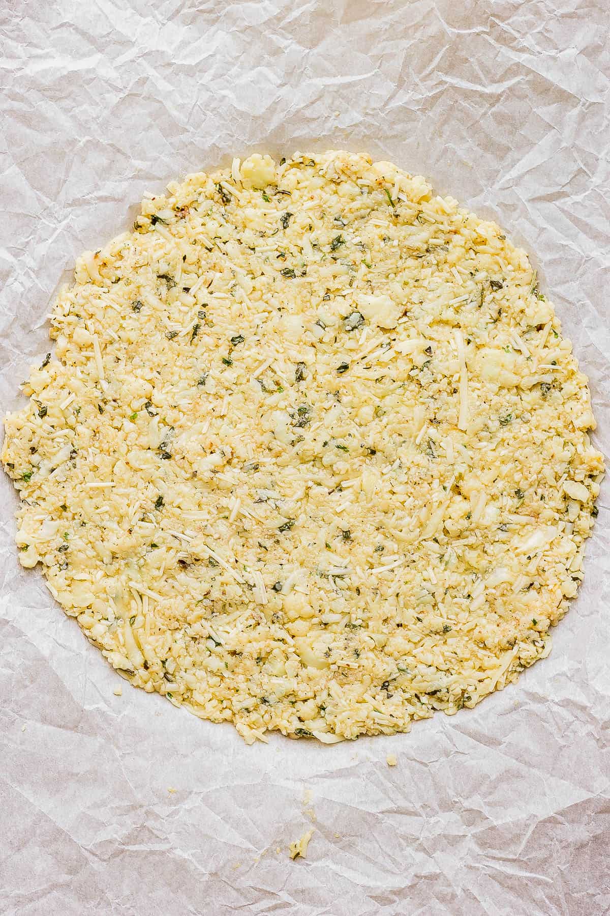 A cauliflower pizza crust before baking on a parchment-lined baking sheet.