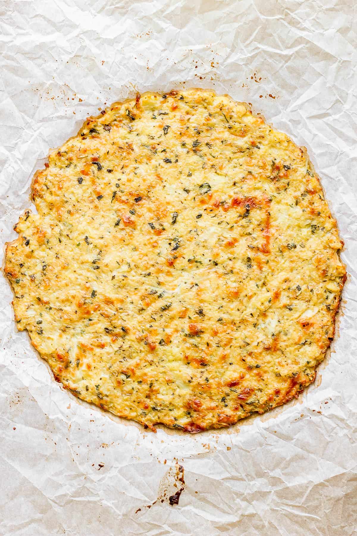 A cooked cauliflower pizza crust on a baking sheet.