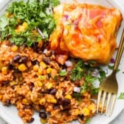 Plate with a slice of chicken enchilada casserole, salsa rice and fresh cilantro on it.