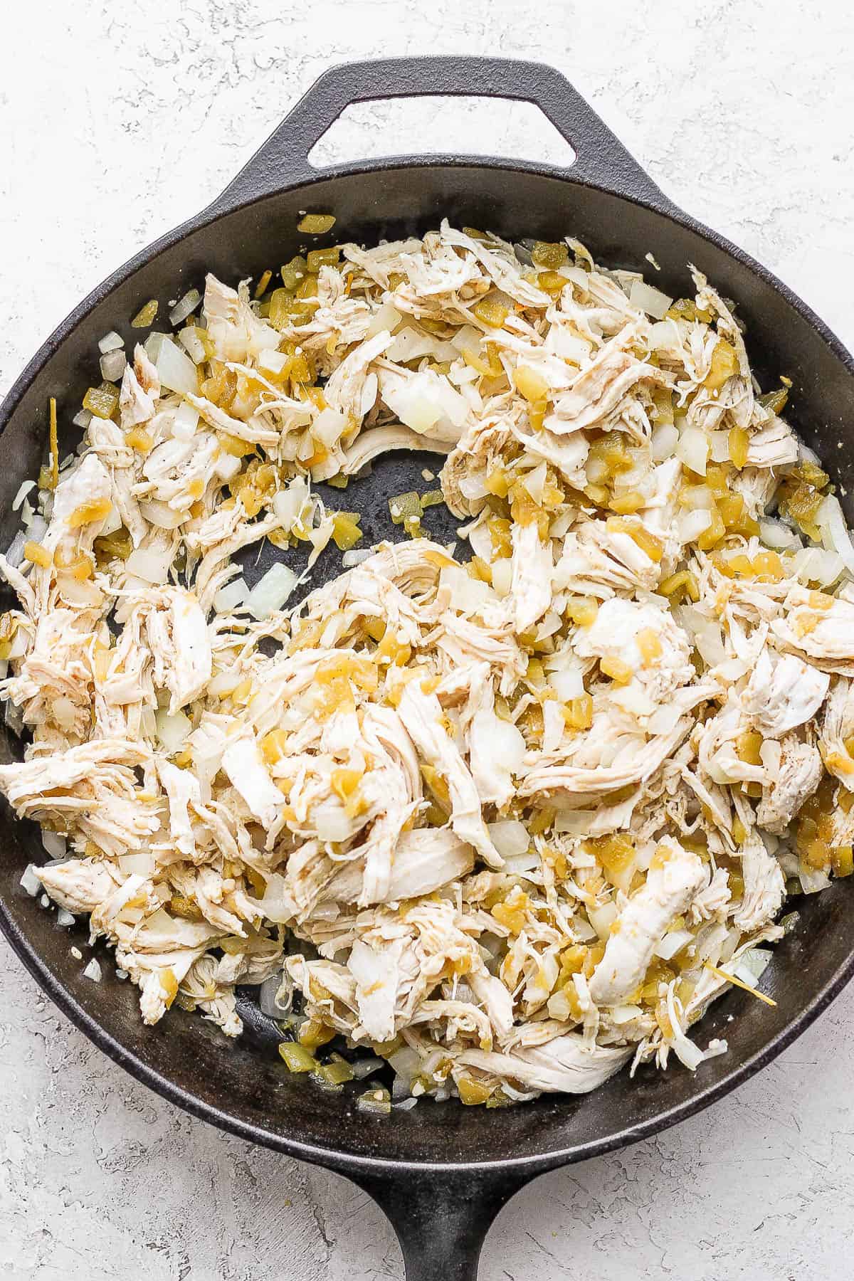 Onion, garlic, green chilis, shredded chicken, and spices in a cast iron skillet.