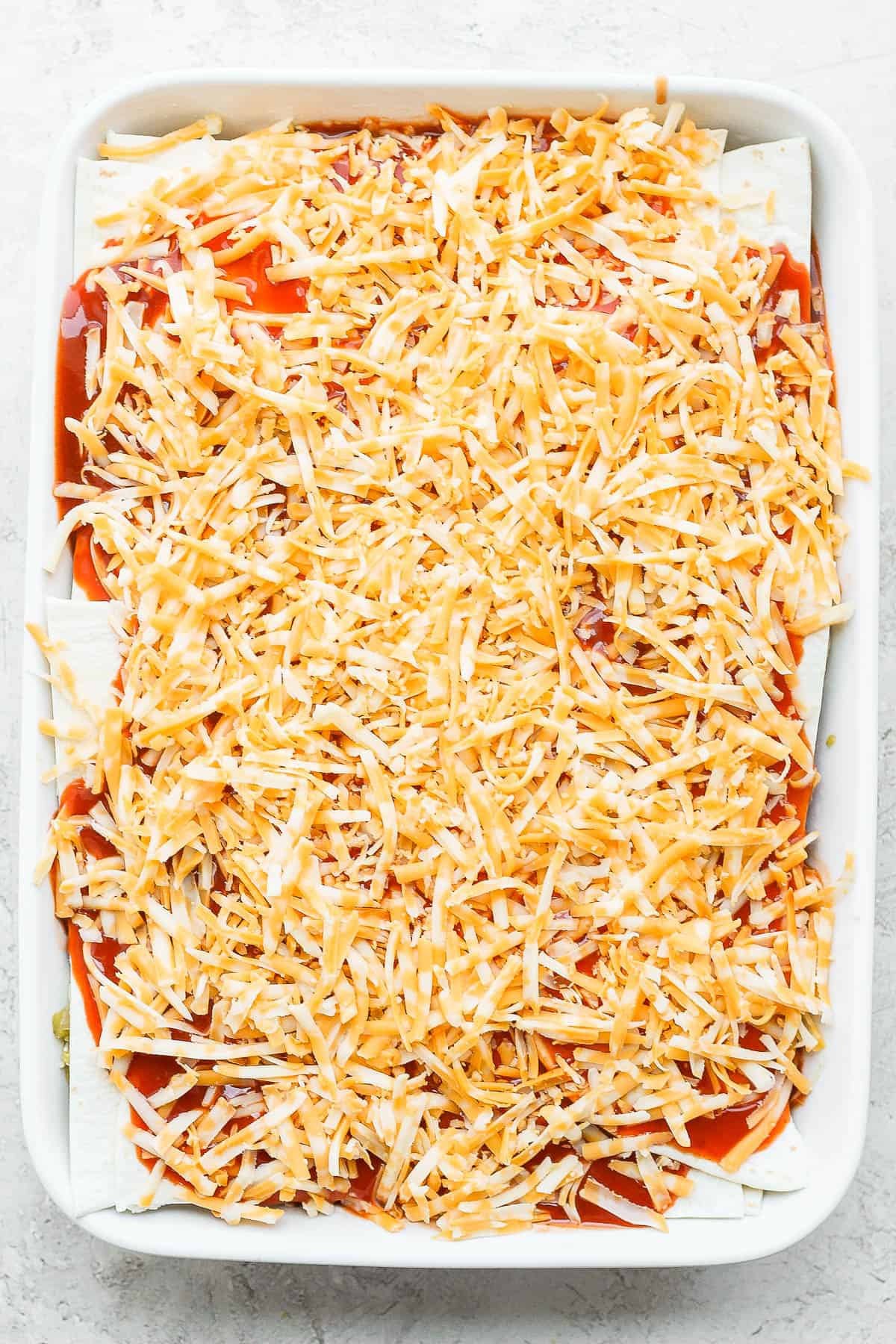 A fully layered chicken enchilada casserole before baking.