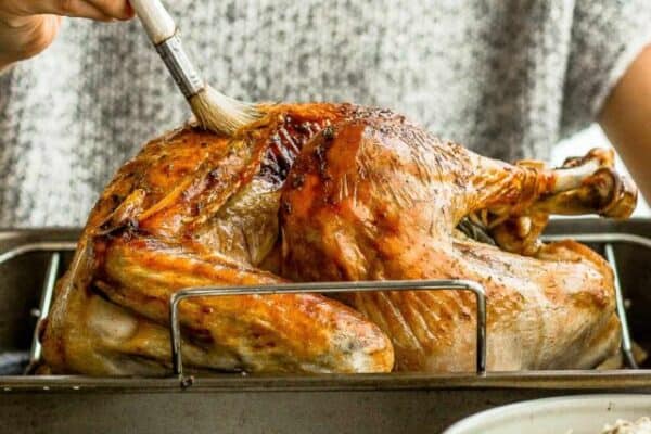 A fully cooked turkey on a roasting rack being brushed with butter.