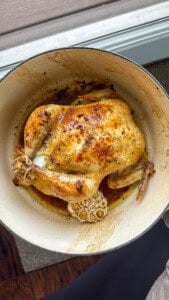 Someone holding a dutch oven with oven mitts and inside in a whole roasted chicken.