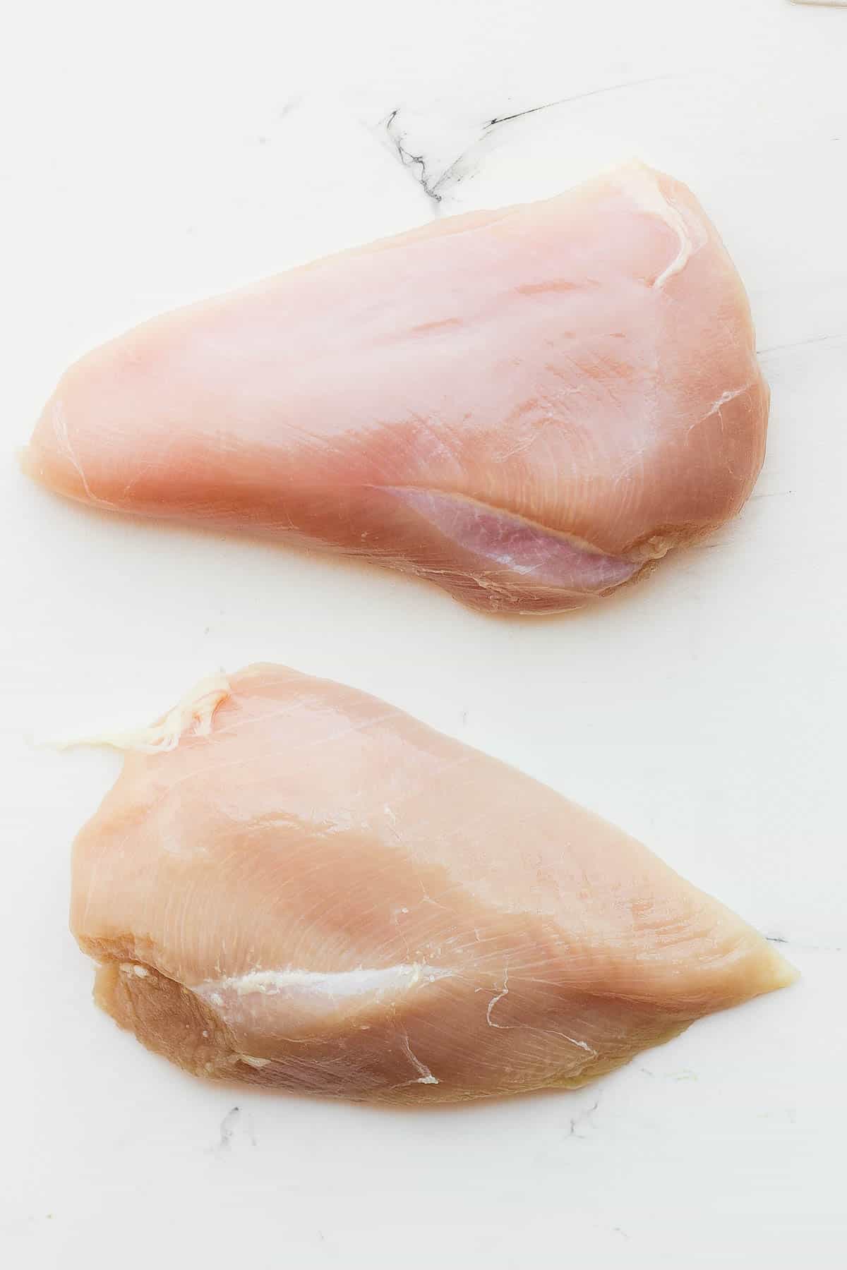 Two raw chicken breasts on a white cutting board.