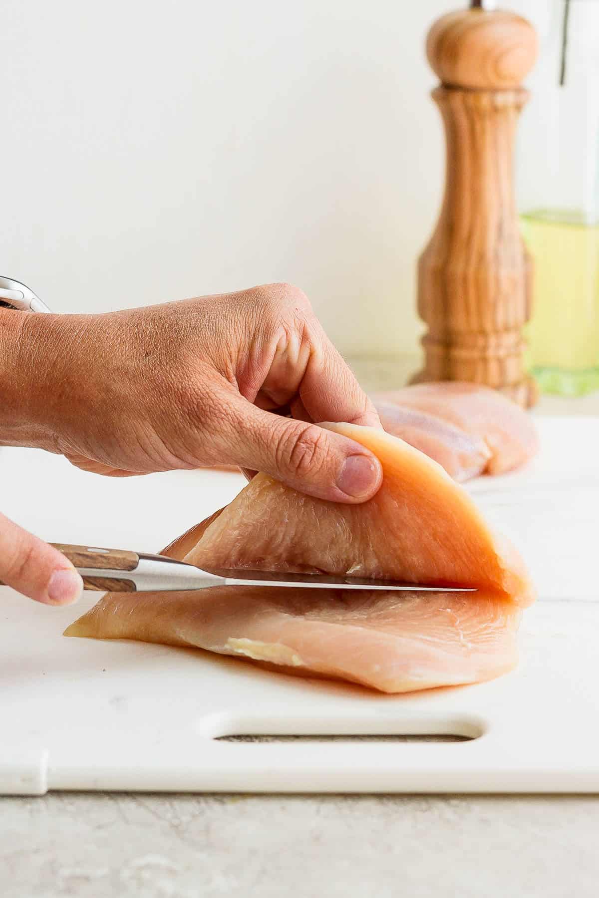 A chicken breast being cut, lengthwise, to make chicken cutlets.