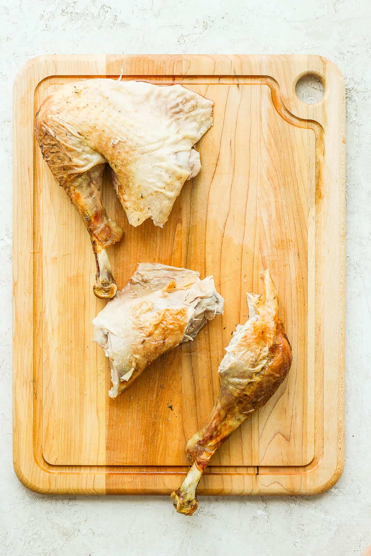 One full turkey leg on the cutting board and one leg that has been separated into a thigh and drumstick.