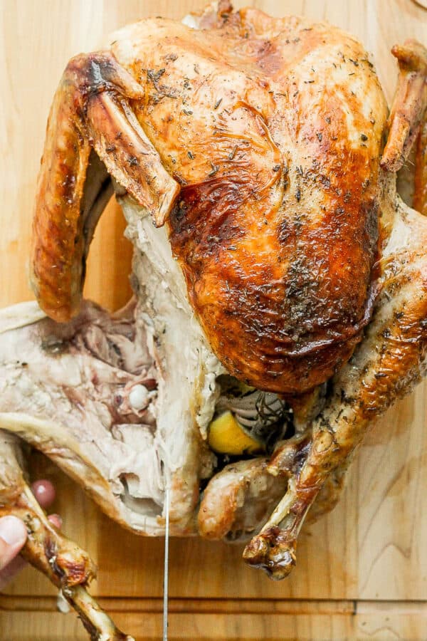 Top shot of a whole, cooked turkey on a cutting board and someone is removing the leg as they begin to carve the turkey.