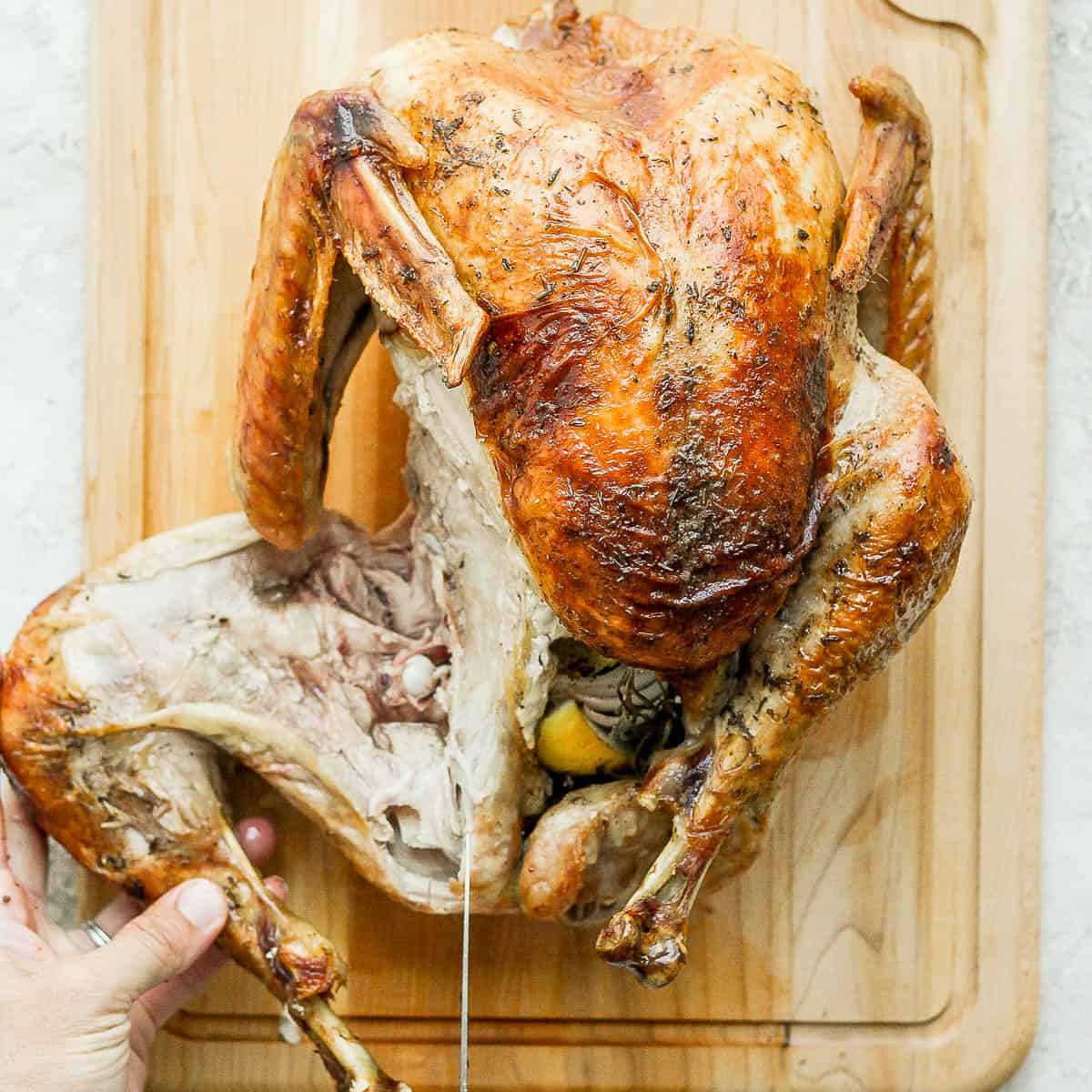 The leg of the turkey being cut off the turkey on a cutting board.