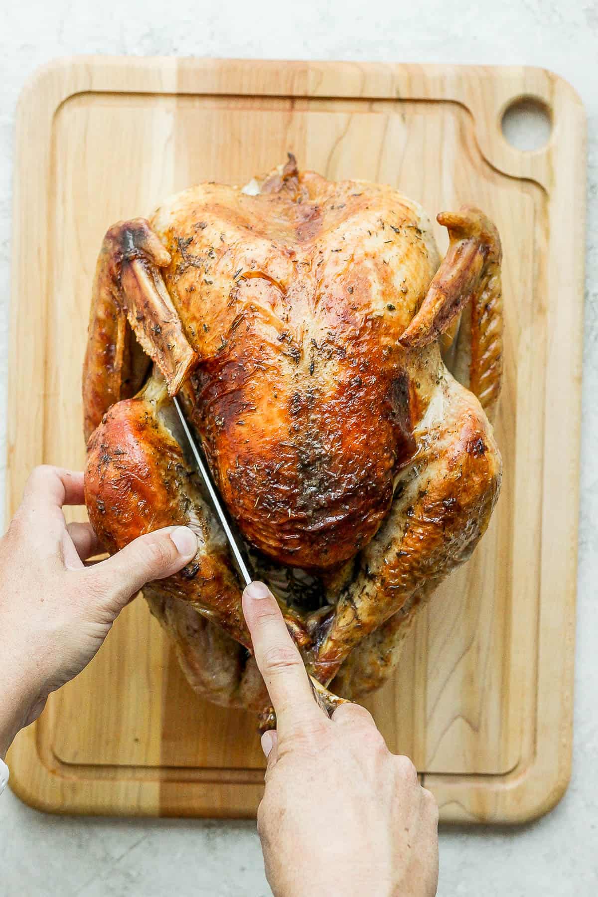 A large, sharp knife cutting the skin between the leg and breast of the turkey.