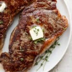 A sous vide steak on a plate with a pad of butter and herbs next to it.